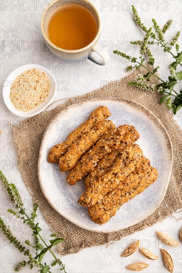 Crumble cookies with seasme and almonds on ceramic plate with cup of green tea and linen textile on