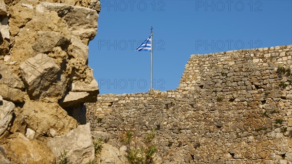 Part of an old fortress wall with a waving Greek flag and blue sky, Chlemoutsi, High Medieval