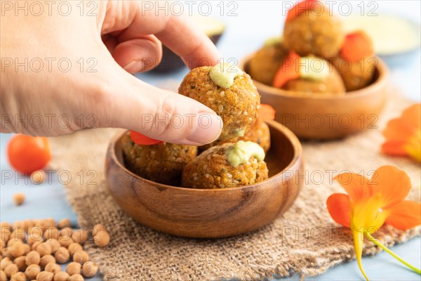 Falafel with guacamole on blue wooden background and linen textile with hand. Side view, close up,