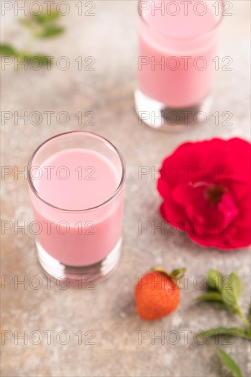 Sweet strawberry liqueur in glass on a gray concrete background and orange textile. side view,
