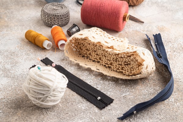Sewing accessories: scissors, thread, thimbles, braid on brown concrete background. Side view,