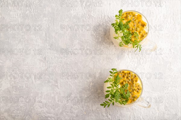 Yogurt with passionfruit and marigold microgreen in glass on gray concrete background. Top view,