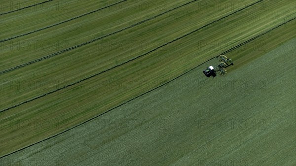 Farmer cutting grass to straight rows with tractor and large roundabout rake, drone shot, Upper