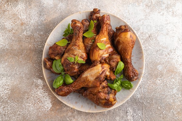 Smoked chicken legs with herbs and spices on a ceramic plate on a brown concrete background. Top