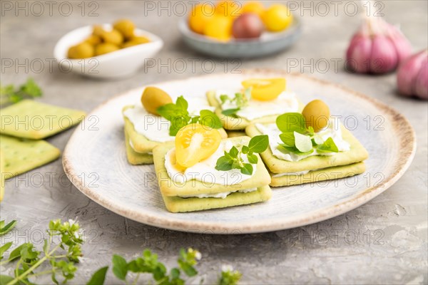 Green cracker sandwiches with cream cheese and cherry tomatoes on gray concrete background. side