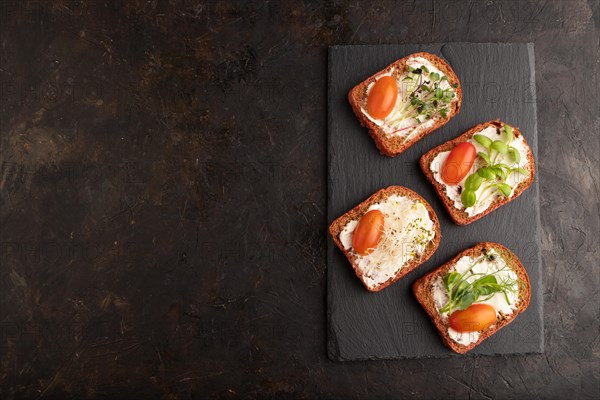 Red beet bread sandwiches with cream cheese, tomatoes and microgreen on black concrete background.