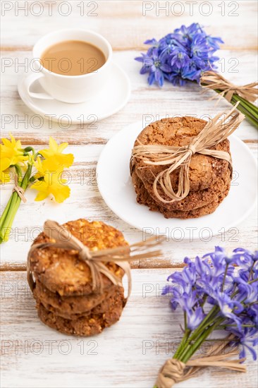 Oatmeal cookies with spring snowdrop flowers bluebells, narcissus and cup of coffee on white wooden