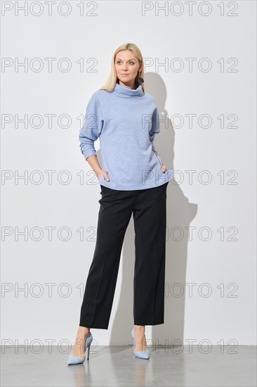 A modern fashion model posing with hands in pockets of classic black trousers wearing a stylish
