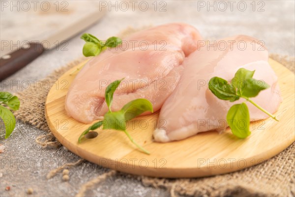 Raw chicken breast with herbs and spices on a wooden cutting board on a brown concrete background.