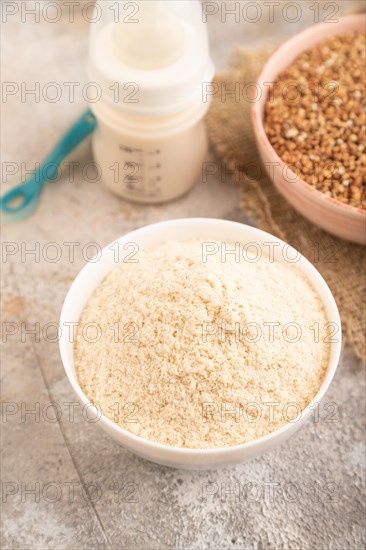Powdered milk and buckwheat baby food mix, infant formula, pacifier, bottle, spoon on brown