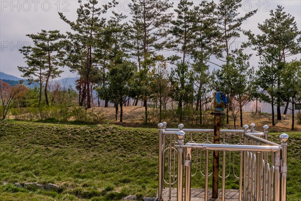 Old hand crank used to open small flood gate in public park with grove of evergreen trees in