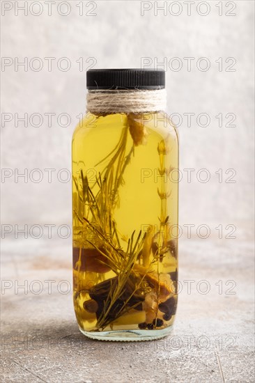 Sunflower oil in a glass jar with various herbs and spices, lavender, sesame, rosemary on a brown