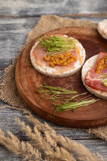 Puffed rice cake sandwiches with jerky salted meat, carrot microgreen on gray wooden background and