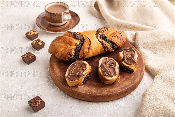 Homemade sweet bun with chocolate cream and cup of coffee on a gray concrete background and linen