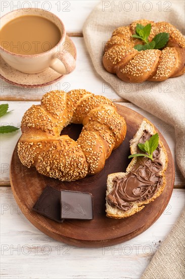 Homemade sweet bun with chocolate cream and cup of coffee on a white wooden background and linen