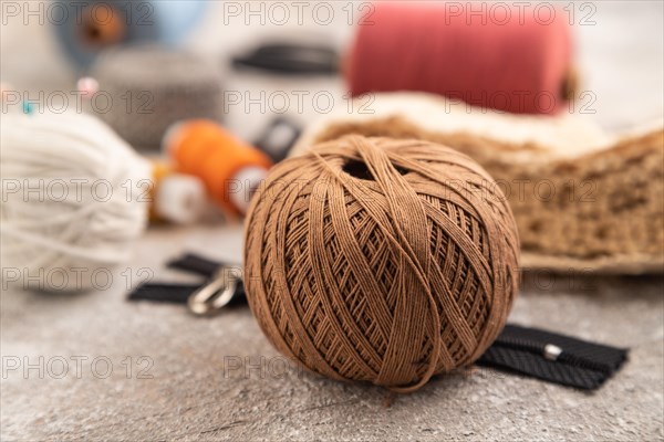 Sewing accessories: scissors, thread, thimbles, braid on brown concrete background. Side view,
