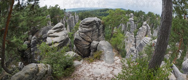 A panoramic view over bizarre rock structures surrounded by forest under a partly cloudy sky,