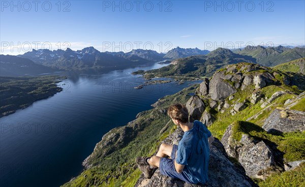 Mountaineer sitting on the summit of Dronningsvarden or Stortinden, behind mountains and fjord