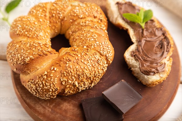 Homemade sweet bun with chocolate cream and cup of coffee on a white wooden background and linen