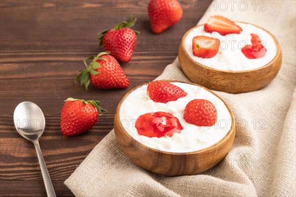 Grained cottage cheese with strawberry jam on brown wooden background and linen textile. side view,