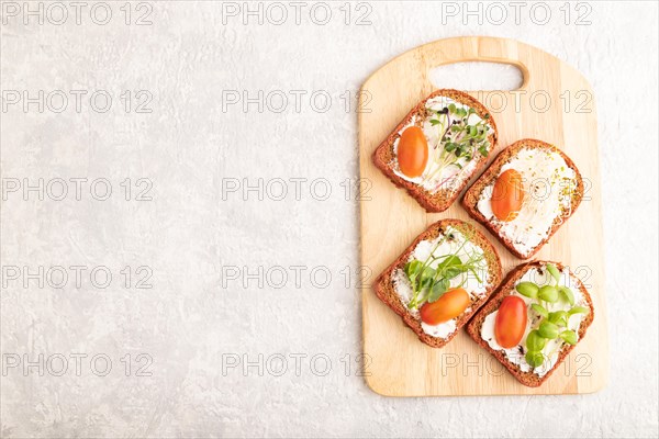 Red beet bread sandwiches with cream cheese, tomatoes and microgreen on gray concrete background.