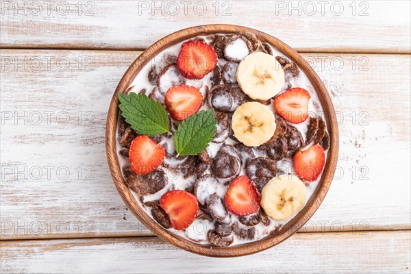 Chocolate cornflakes with milk and strawberry in wooden bowl on white wooden background. Top view,