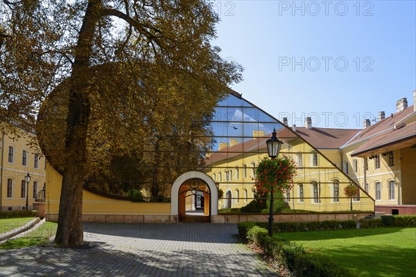 A facade combining historical architecture and modern glass structures in a paved courtyard,
