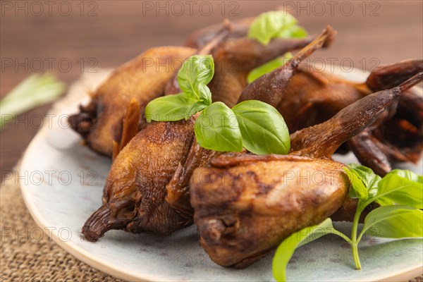 Smoked quails with herbs and spices on a ceramic plate with linen textile on a brown wooden