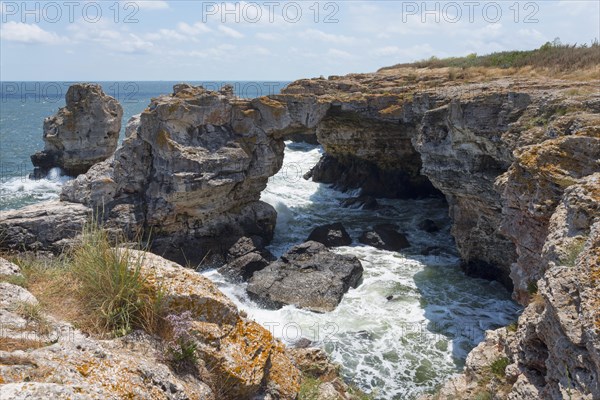 Rugged rock formations and natural arch on a stormy coast against a bright blue sky, rock arch,