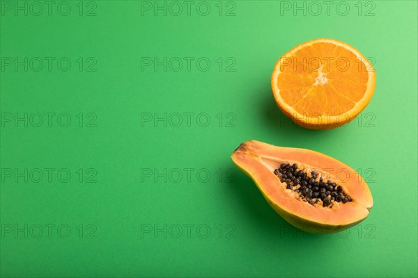 Ripe cut papaya and orange on green pastel background. Side view, copy space. Tropical, healthy