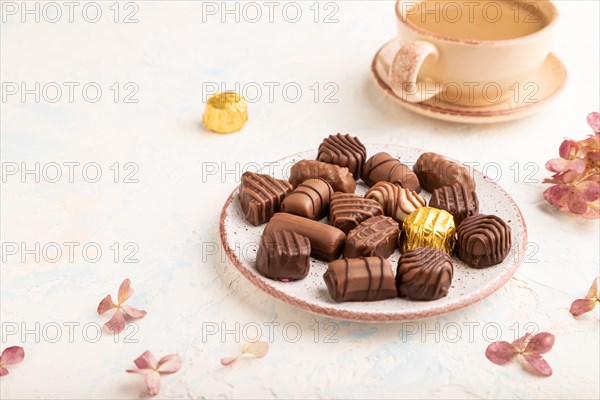 Chocolate candies with cup of coffee and hydrangea flowers on a white concrete background. side