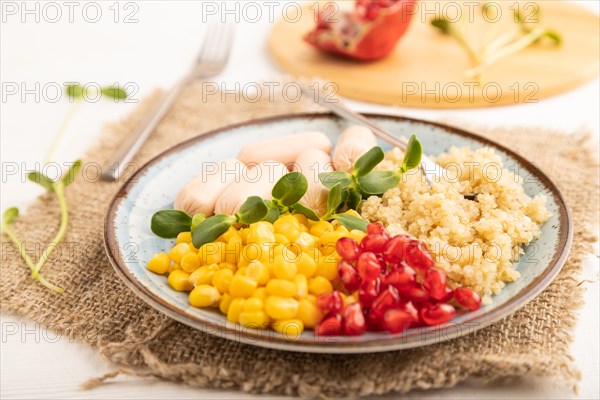 Mixed quinoa porridge, sweet corn, pomegranate seeds and small sausages on white wooden background.