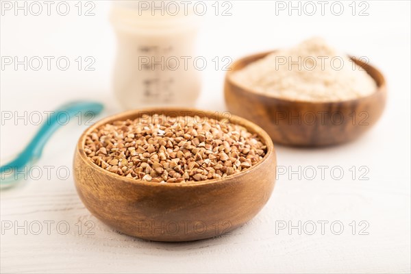Powdered milk and buckwheat baby food mix, infant formula, pacifier, bottle, spoon on white wooden