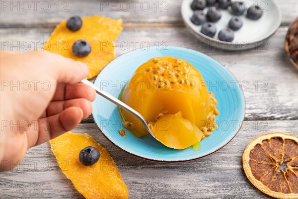 Mango and passion fruit jelly with blueberry with hand on gray wooden background. side view, close