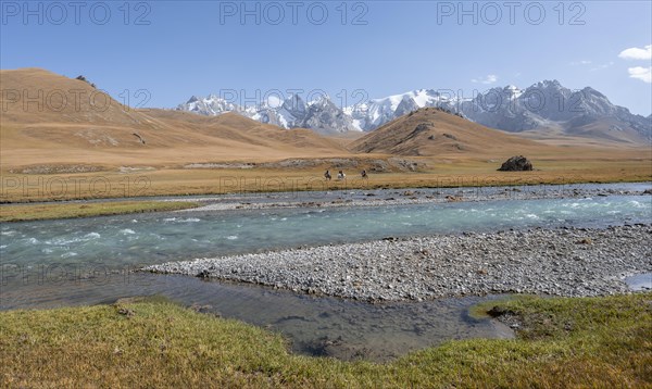 Riders on horses on the river bank, mountain landscape with yellow meadows and river Kol Suu,