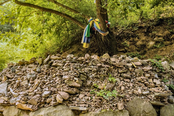 Colorful clothes wrapped around a tree beside numerous pebble stacks and loose stones in South