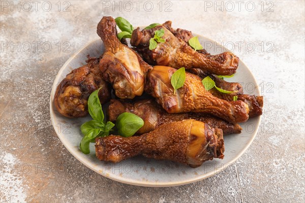 Smoked chicken legs with herbs and spices on a ceramic plate on a brown concrete background. Side