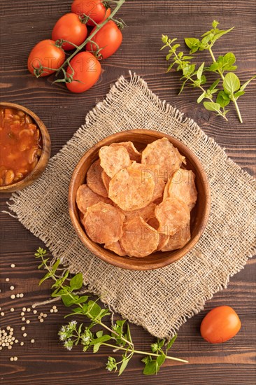 Slices of dehydrated salted meat chips with herbs and spices on brown wooden background and linen