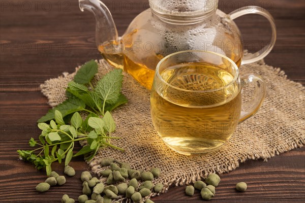 Green oolong tea with herbs in glass on brown wooden background and linen textile. Healthy drink