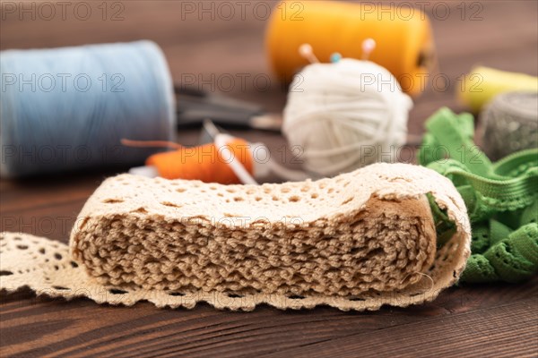 Sewing accessories: scissors, thread, thimbles, braid on brown wooden background. Side view, close