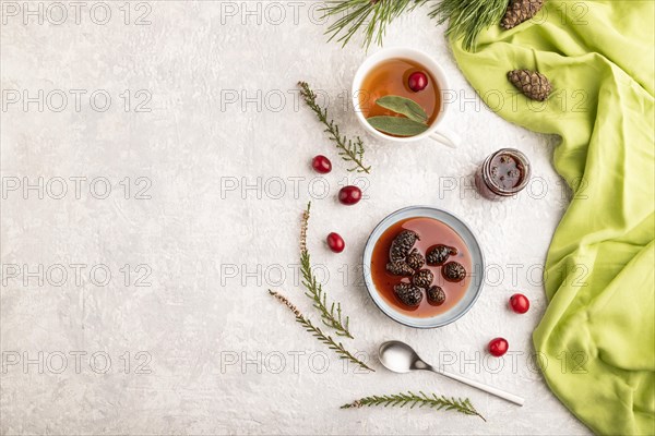 Pine cone jam with herbal tea on gray concrete background and green linen textile. Top view, flat