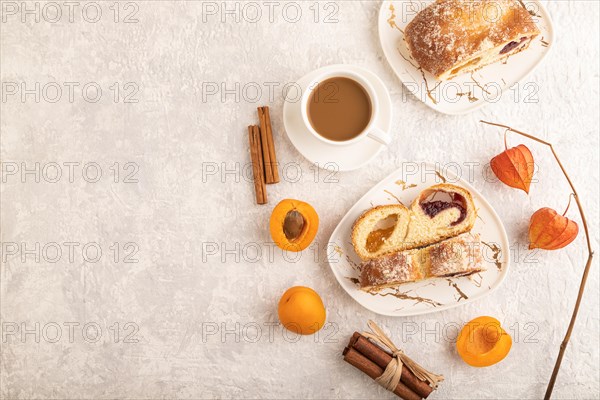 Homemade sweet bun with apricot jam and cup of coffee on gray concrete background. top view, flat