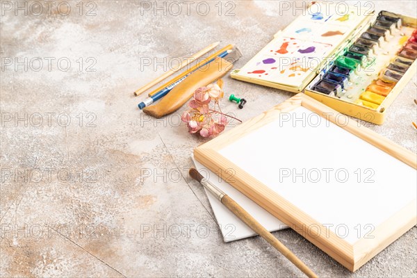 Drawing accessories set: brushes, pencils, watercolor, frame on brown concrete background. Side