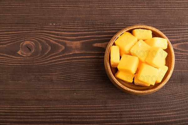 Dried and candied mango cubes in wooden bowls on brown wooden textured background. Top view, flat