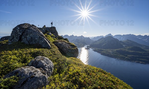 Mountaineer on the summit of Dronningsvarden or Stortinden, behind sea and fjord Umvagsundet,