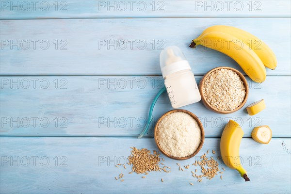 Powdered milk and oatmeal, banana baby food mix, infant formula, pacifier, bottle, spoon on blue