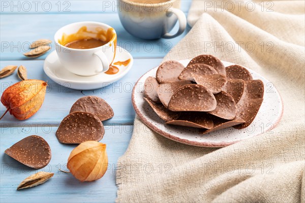Chocolate chips with cup of coffee and caramel on a blue wooden background and linen textile. side