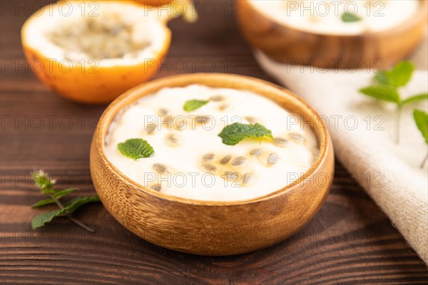 Yoghurt with granadilla and mint in wooden bowl on brown wooden background and linen textile. side
