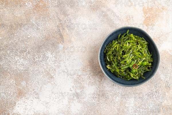 Chuka seaweed salad in blue ceramic bowl on brown concrete background. Top view, flat lay, copy