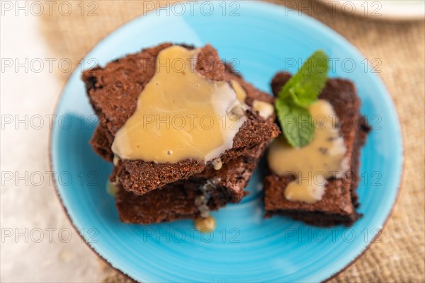 Chocolate brownie with caramel sauce with a cup of coffee on gray concrete background and linen